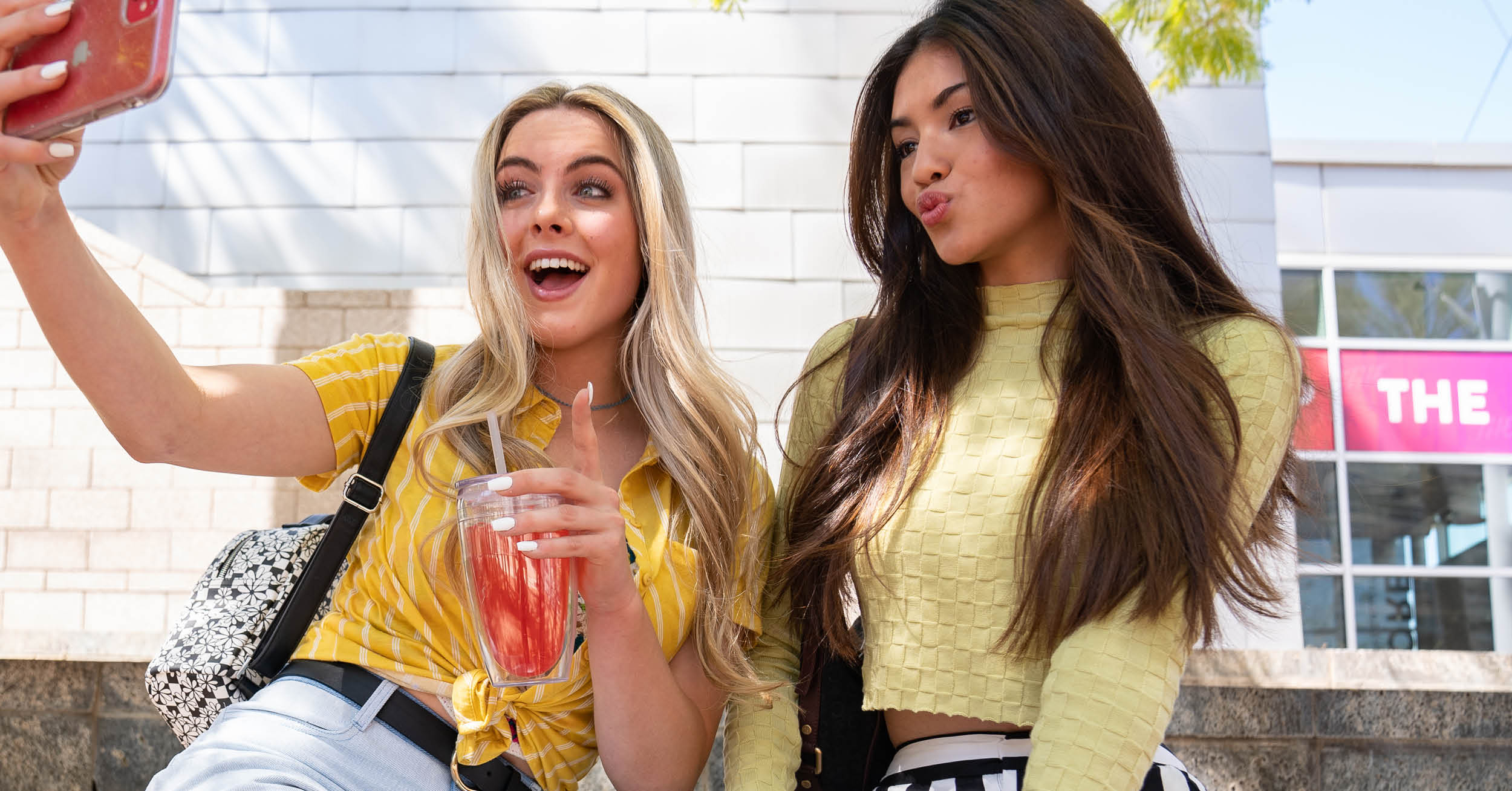 Two teens taking a selfie in front of a storefront